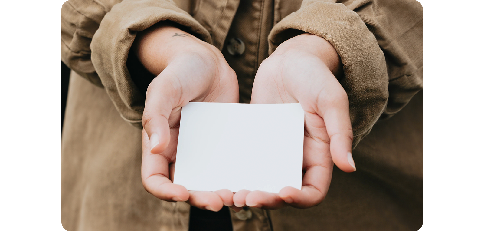 A person in a brown jacket holds a blank white card with both hands, presenting it forward as if offering it to someone. This image is used to symbolize the concept of pre-game communication, emphasizing the importance of setting expectations and objectives before a session begins.