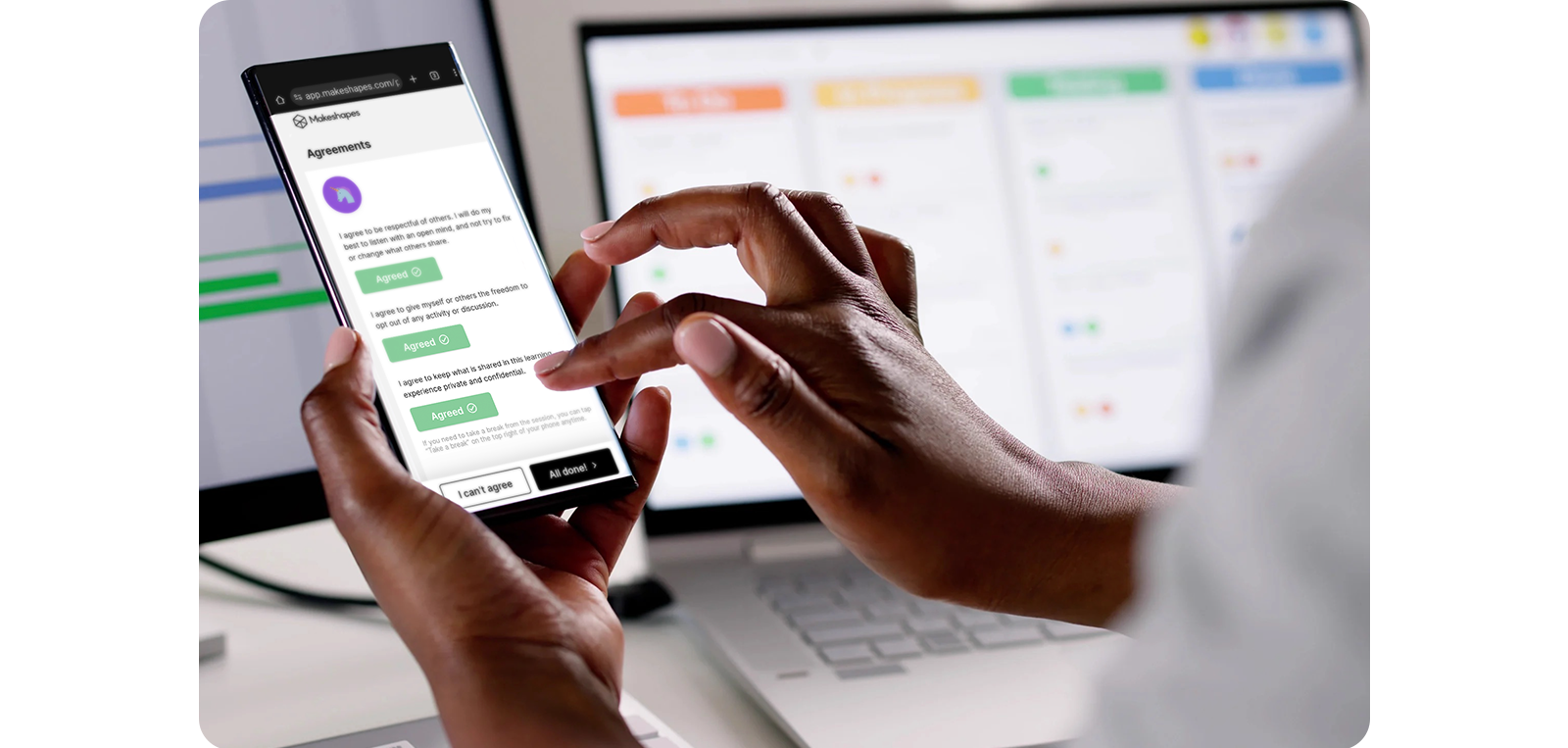 Hands holding a smartphone with an interface open, showing messages about shared agreements, in front of a laptop.